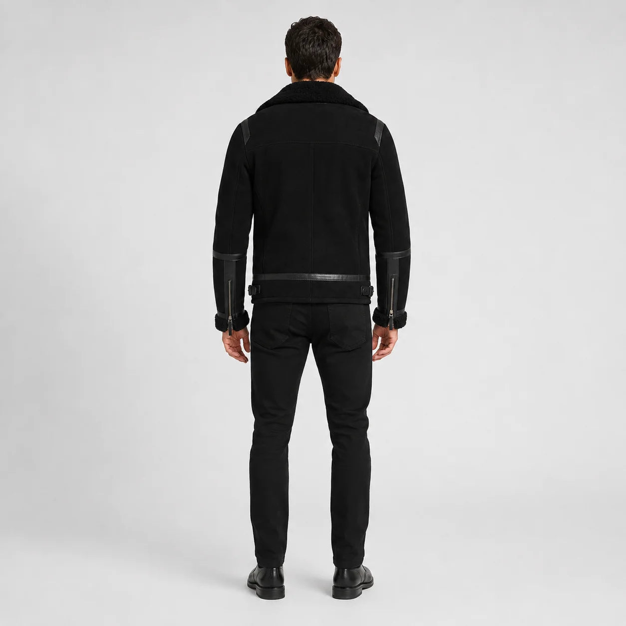 Rear studio view of men’s black aviator jacket showing clean back seams, cuff zips and adjustable waist tabs