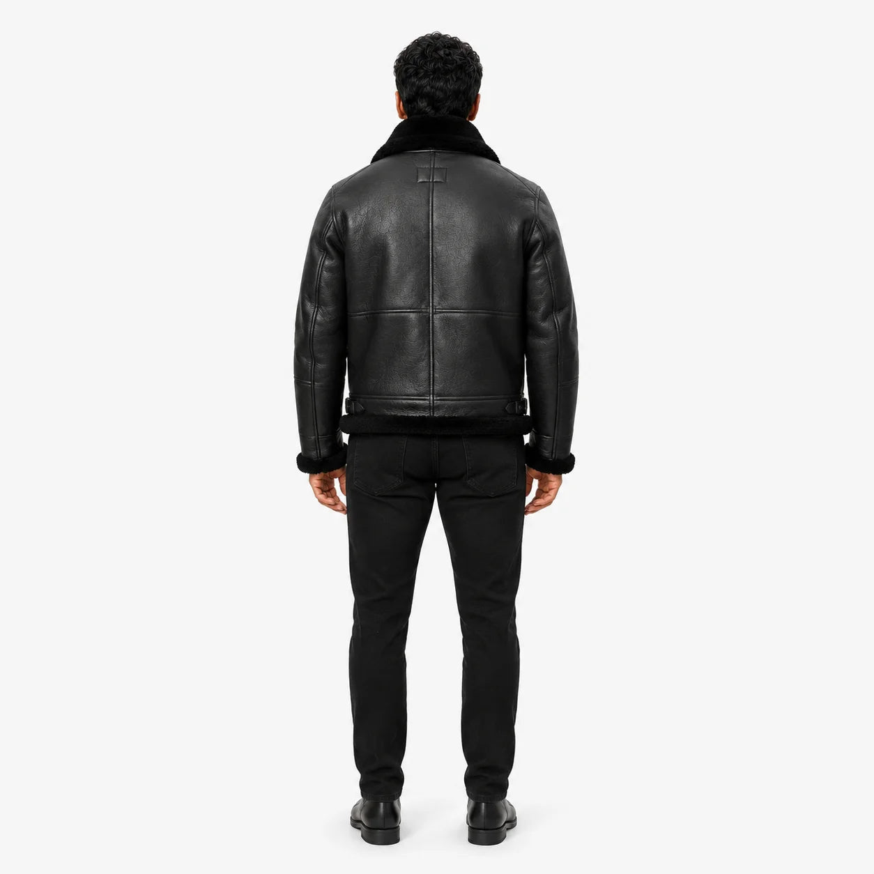 Rear studio view showing textured black leather back panels, black shearling collar, cuffs and trimmed hem