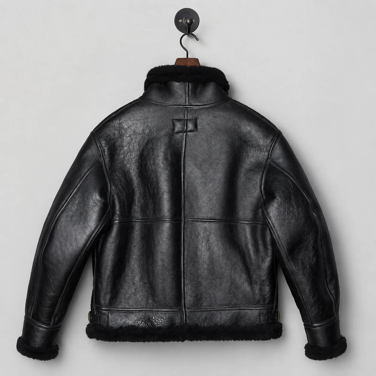 Back hanging view of black sheepskin flight jacket showing central seam, textured leather and shearling hem trim