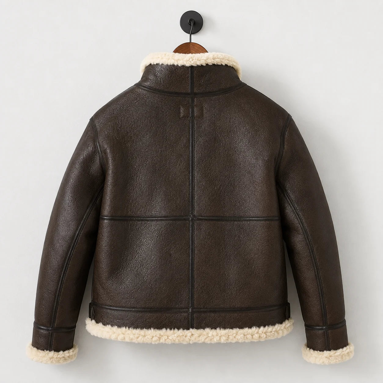 Hanging rear view of men’s brown leather B3 jacket showing central back seam, horizontal panels and cream-trimmed hem.