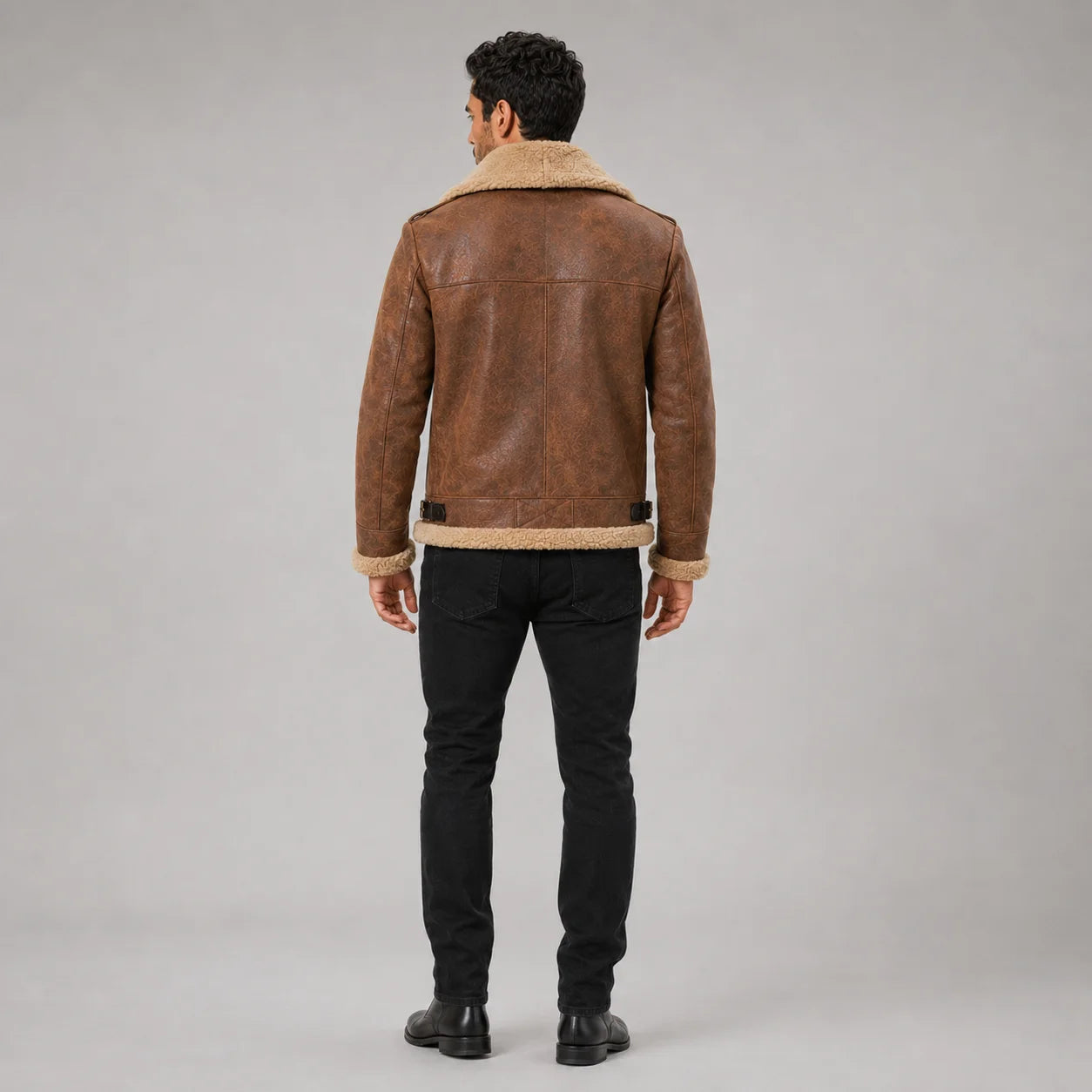 Back studio view showing the brown aviator jacket’s shoulder yoke, centre seam, waist adjusters and cream hem trim.