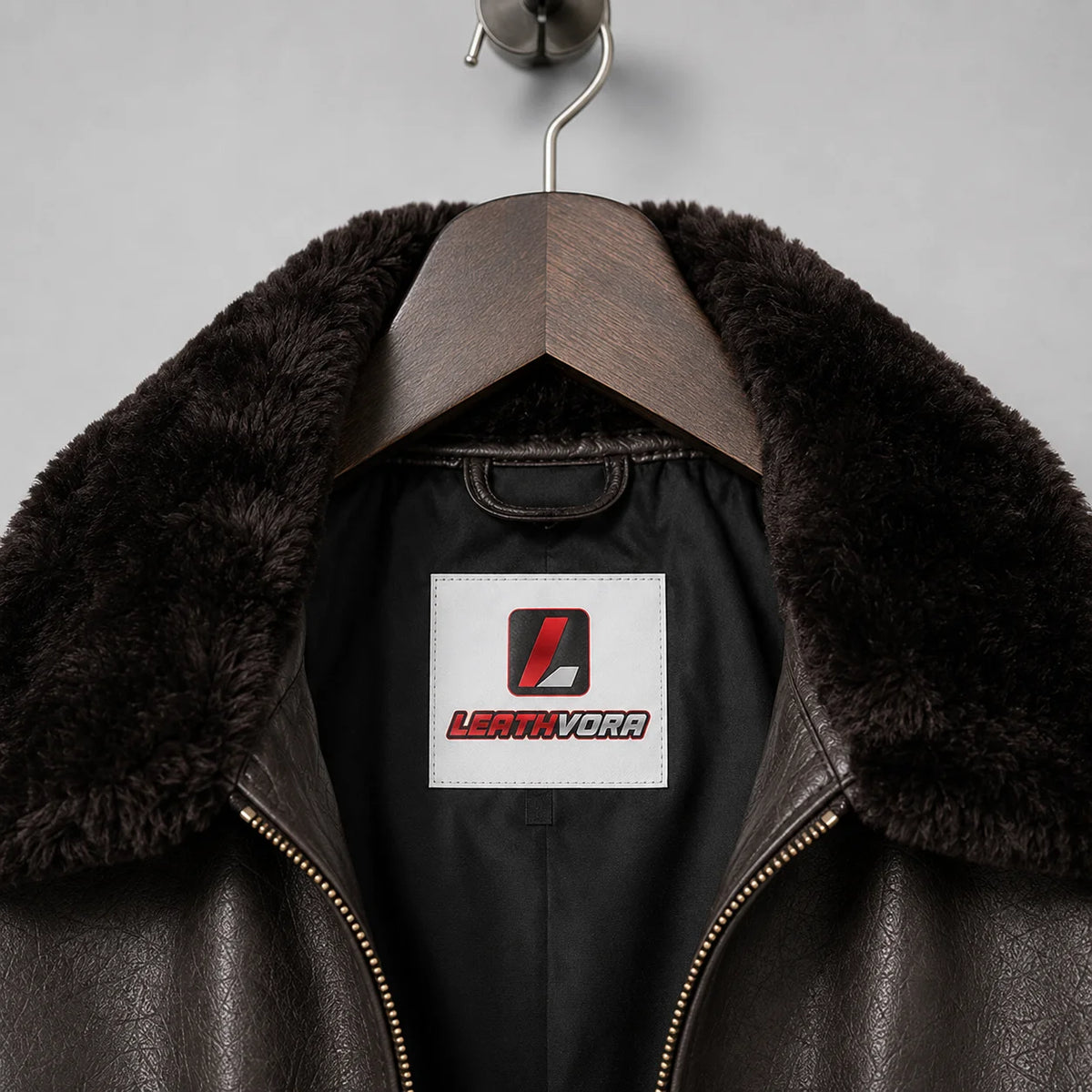 Close-up of dark plush collar, brown textured leather, black inner lining and Leathvora neck label on flight jacket
