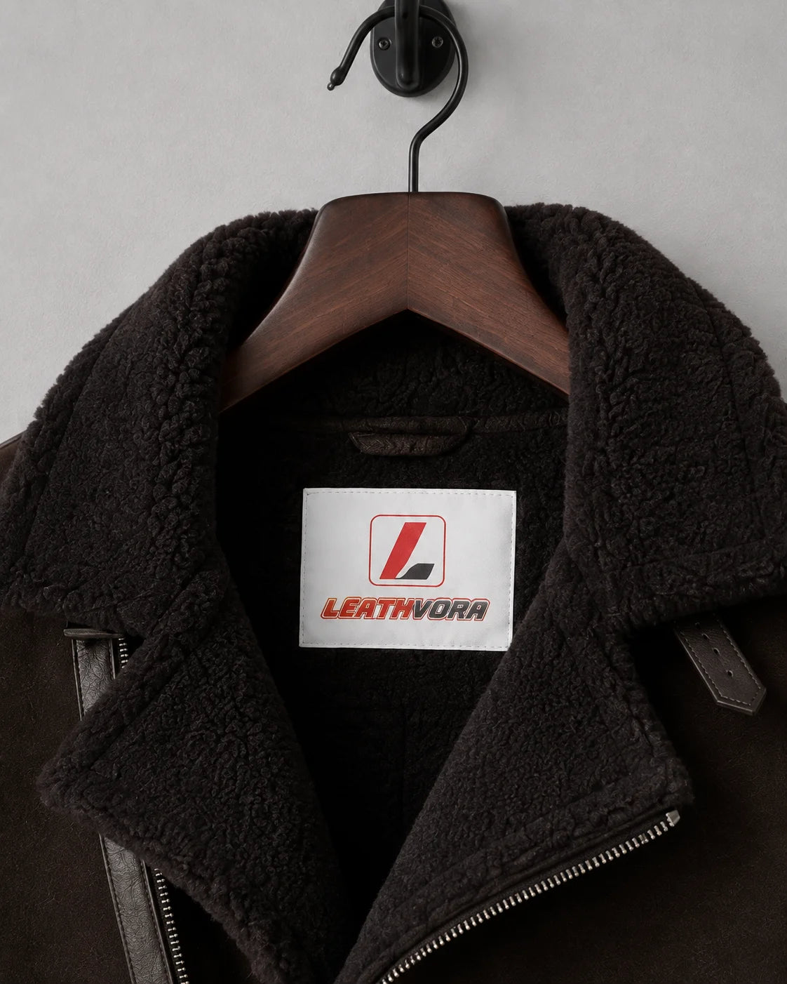 Close-up of dark plush aviator collar, asymmetric zip edge and Leathvora branding inside the brown jacket