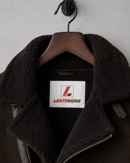 Close-up of dark plush aviator collar, asymmetric zip edge and Leathvora branding inside the brown jacket