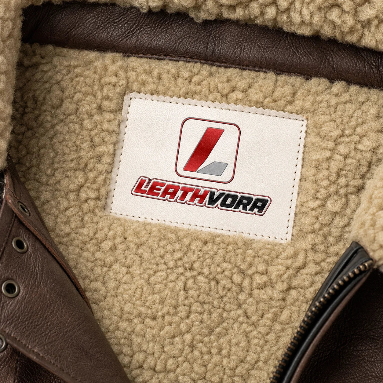 Close-up of cream fleece lining with Leathvora neck patch, brown leather collar straps and front zipper detail