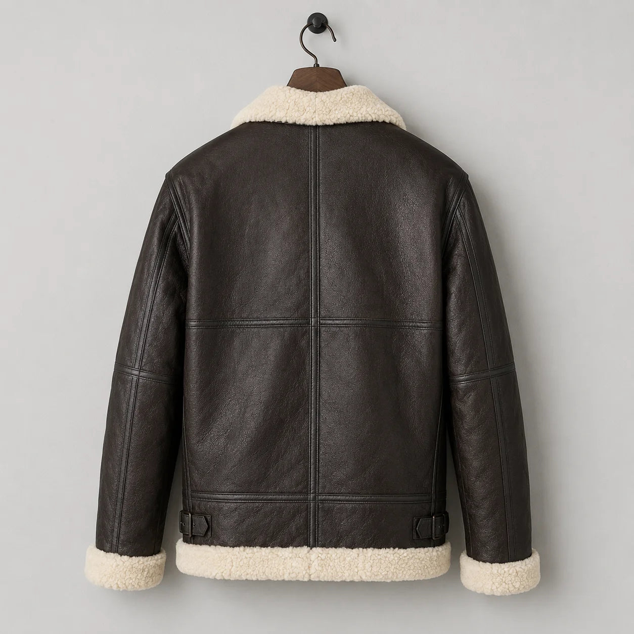 Hanging rear view of dark brown leather flight jacket with cream shearling hem, collar and structured back seams.