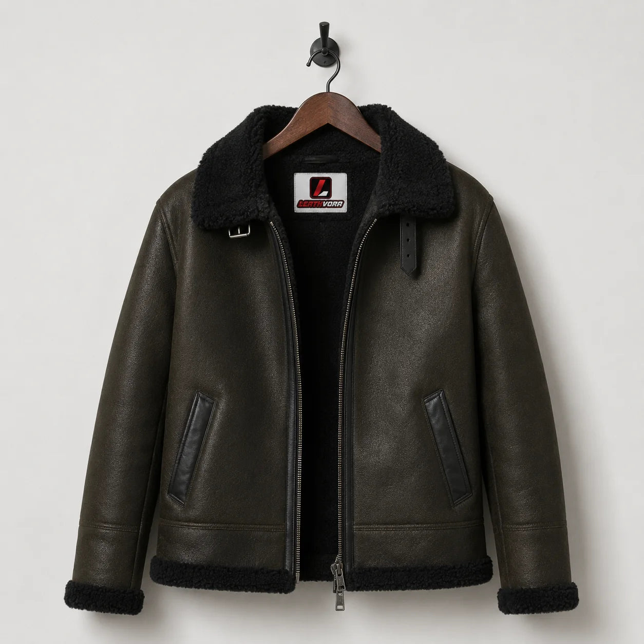 Hanging front view of dark green aviator jacket with black plush lining, collar strap, front zipper and Leathvora label